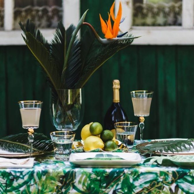 Ein festlich gedeckter Tisch mit tropischen Pflanzen und Obst, umgeben von einer grünen Wand. Sekt und Sektglas Ein festlich gedeckter Tisch mit tropischen Pflanzen und Obst, umgeben von einer grünen Wand.