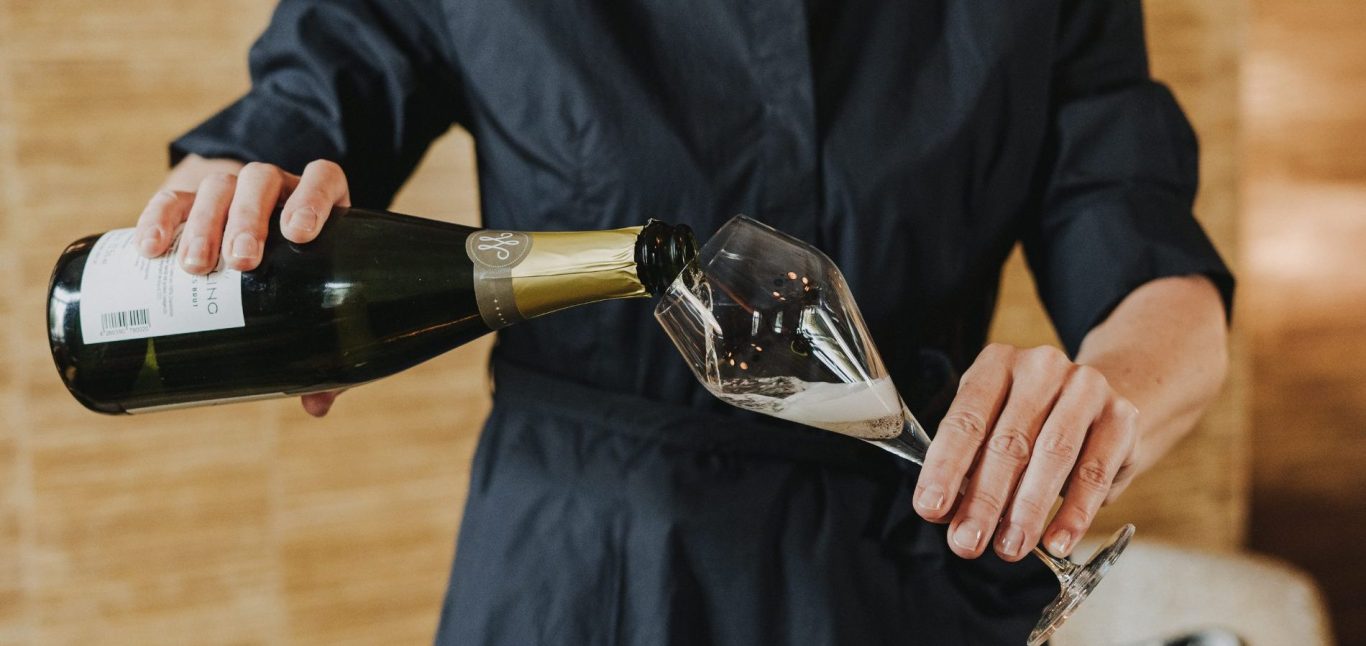 Schaumweinmagazin Nicole Wolbers schenkt Winzersekt Crémant ein Eine Person gießt Sekt aus einer Flasche in ein Glas.